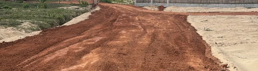 Terraplenagem de acesso executada pela RICCO à beira-mar, com a via já conformada e a praia ao fundo.