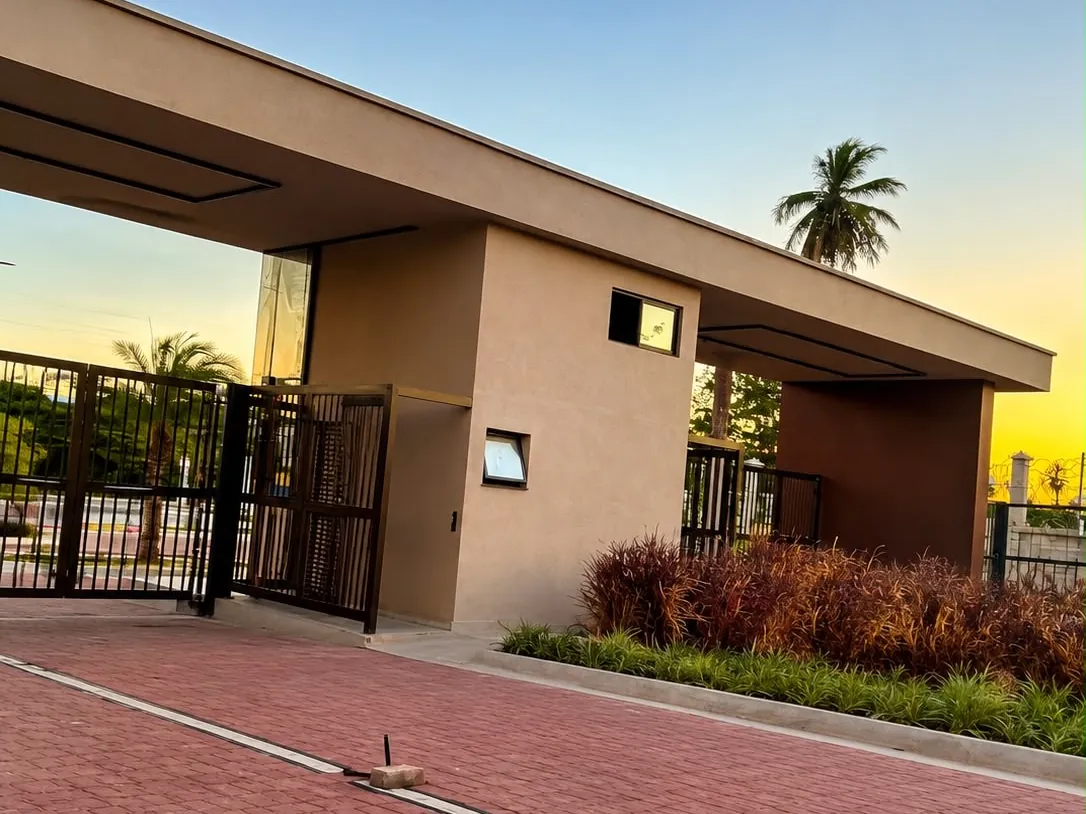 Portaria de loteamento entregue pela RICCO ao anoitecer, com marquise em concreto e pavimentação intertravada.
