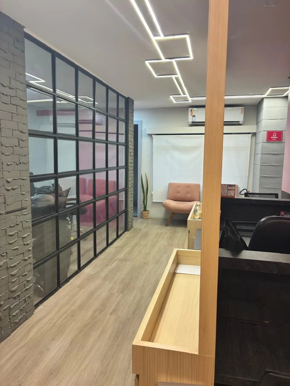 Interior comercial com divisória de vidro em esquadria preta, parede de tijolo aparente pintado e iluminação linear no forro.