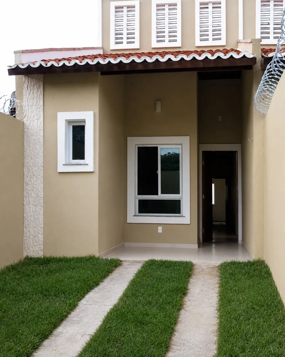 Fachada de residência entregue pela RICCO, com passeio em concreto, grama e esquadrias brancas.